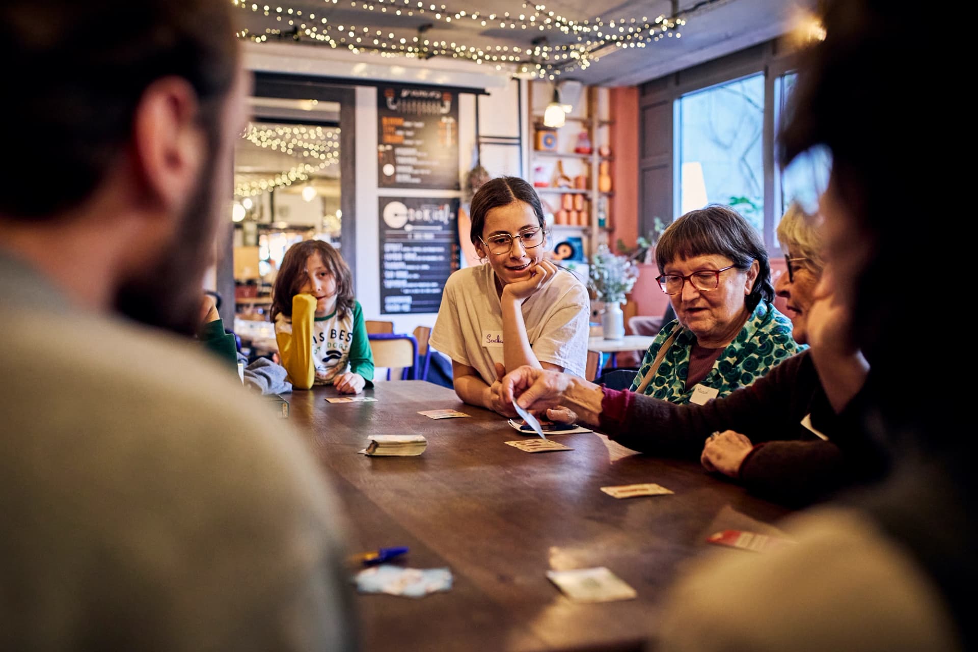 Grande table intergénérationnelle de jeux de société dans un café à Montreuil